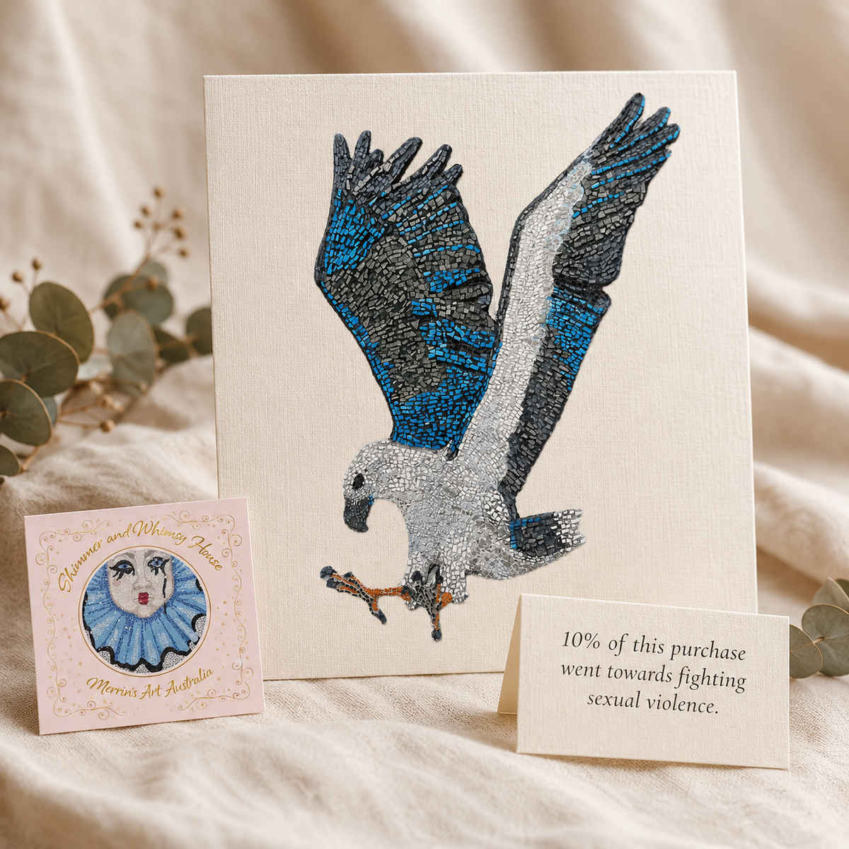 Willow White-bellied Sea Eagle mosaic postcard displayed beside the Shimmer and Whimsy House logo and an elegant card reading “10% of this purchase went towards fighting sexual violence,” styled softly on linen to show meaningful art, giving back and purpose-led gifting.