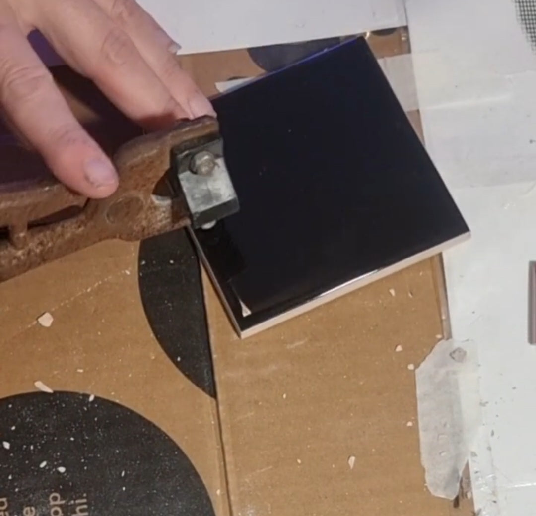 Load video: Video still showing black tiles being cut into strips, then nipped into small, detailed pieces suitable for mosaic work. Hands and tile-cutting tools are seen actively shaping the tiles on a workspace.