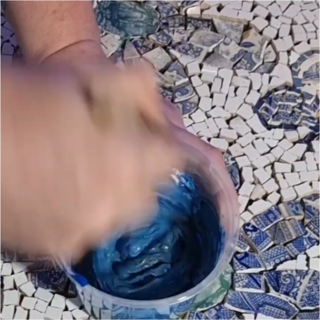 Load video: Time-lapse video of blue-grey grout being applied to the custom daisy mosaic paver, spreading and smoothing it over the tiles before cleaning to reveal the completed design.