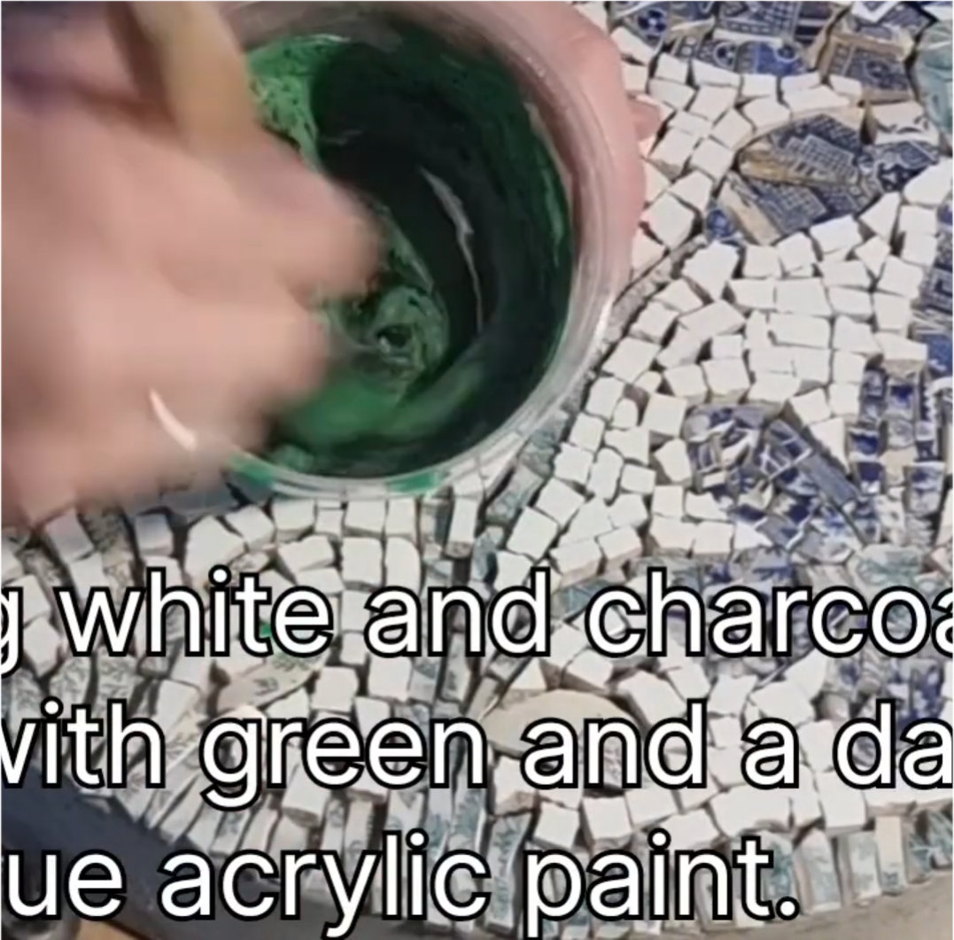 Load video: Time-lapse video of green grout being applied to the custom daisy mosaic paver, spreading and smoothing the grout over the tiles before cleaning to reveal the finished design.