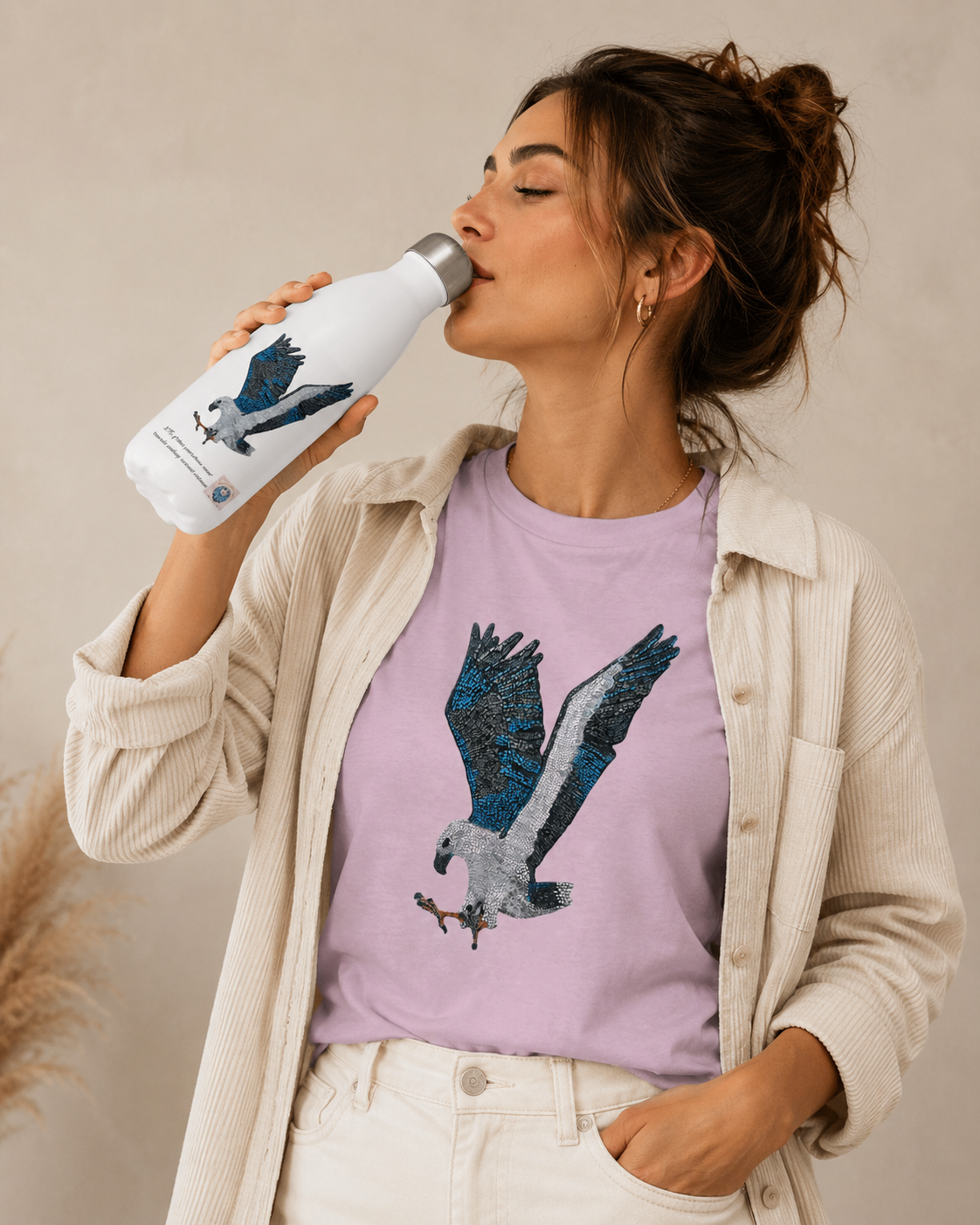 Model drinking from the Willow White-bellied Sea Eagle stainless steel water bottle while wearing a matching Willow mosaic t-shirt in a casual studio lifestyle image.