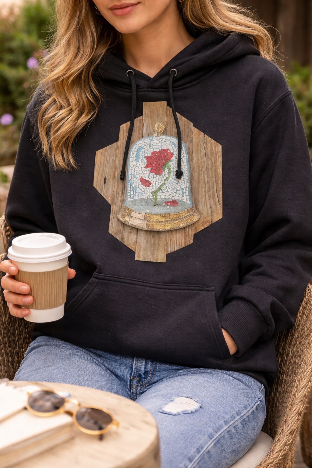 Person wearing a black hoodie with a cursed rose mosaic design, holding a coffee cup outdoors.