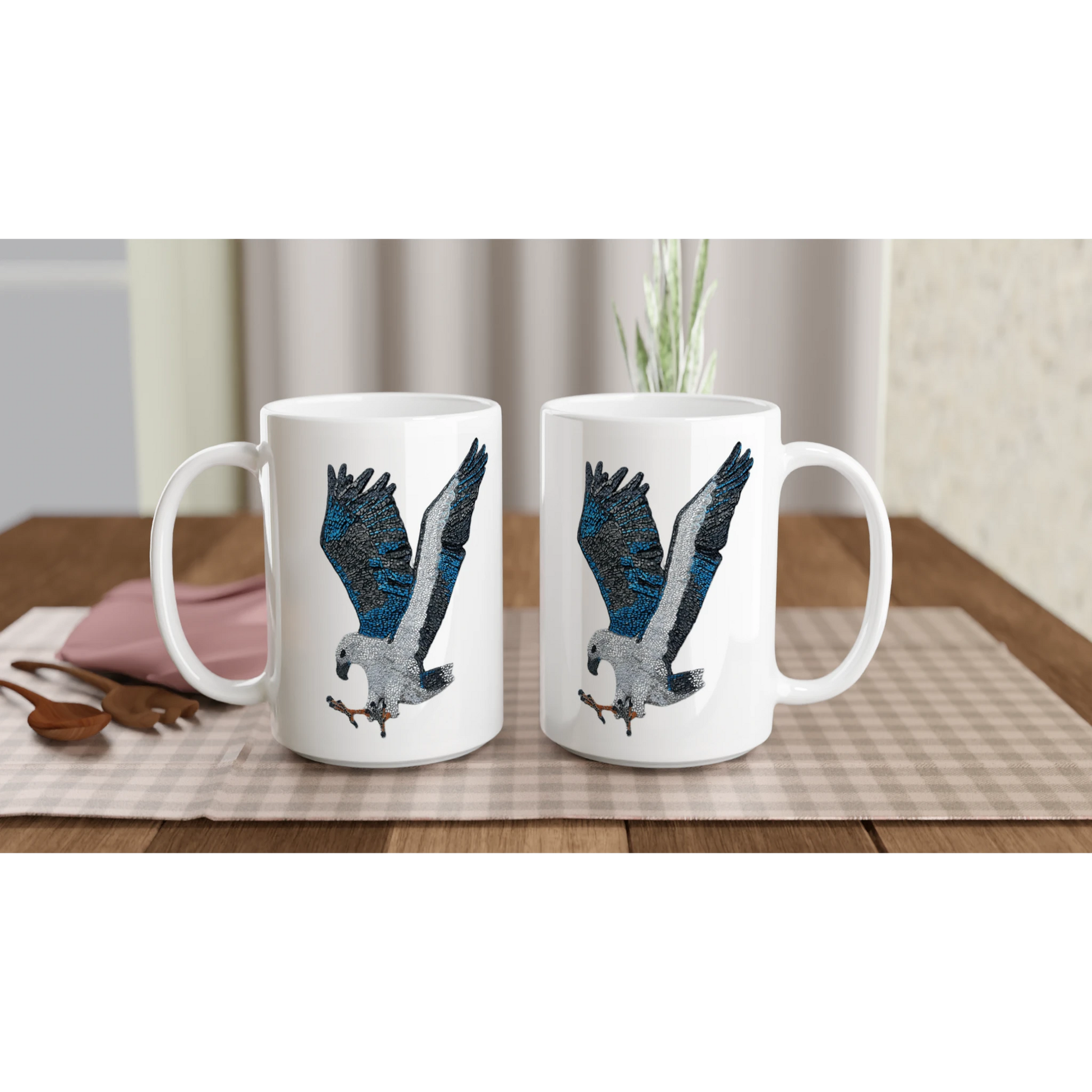 Willow the white-bellied sea eagle mosaic design printed on white ceramic mugs displayed in a lifestyle setting on a gingham set up dining table
