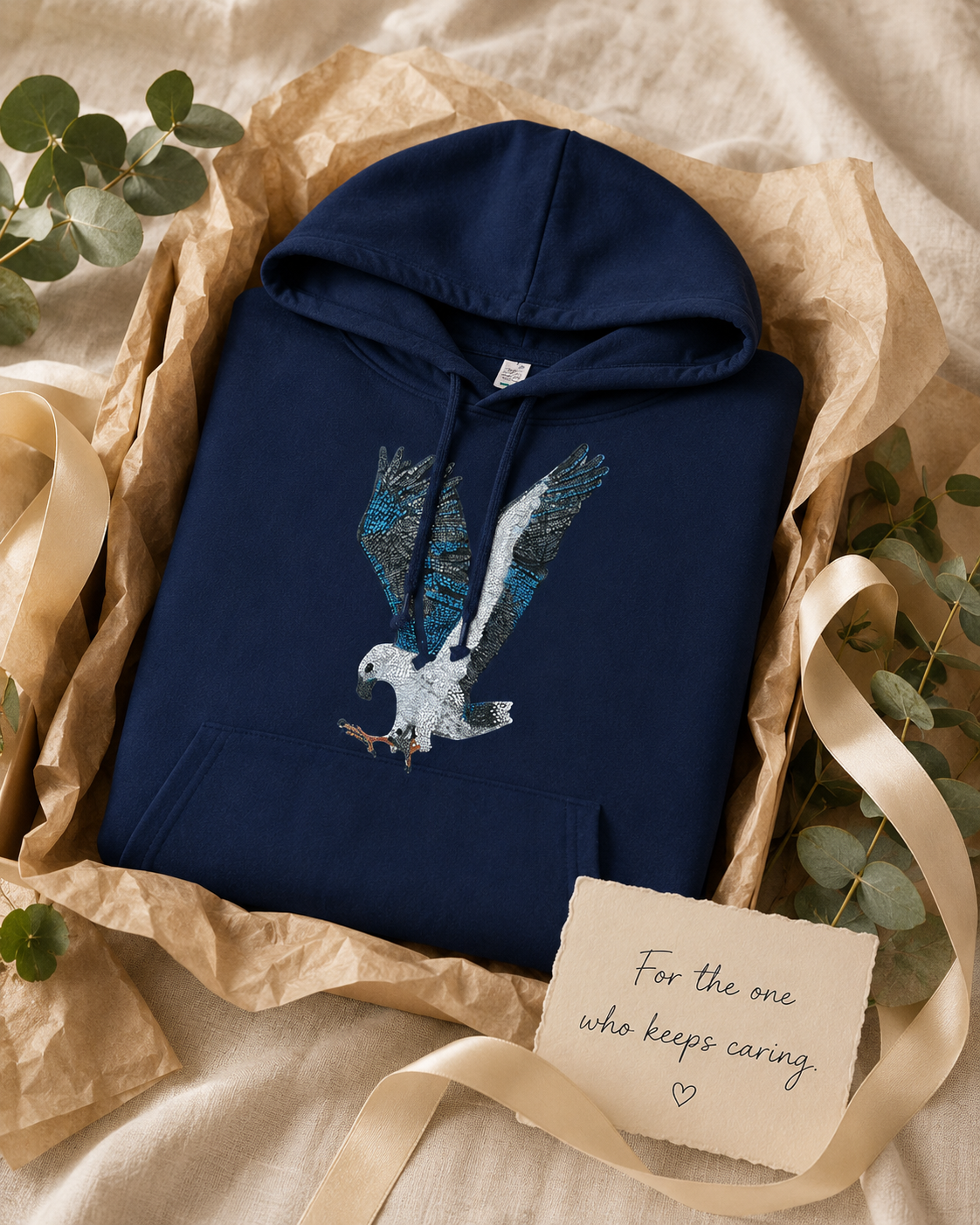 Gift-style flat lay of the navy Willow hoodie folded with recycled paper, soft ribbon, eucalyptus, and a handwritten card reading “For the one who keeps caring.”