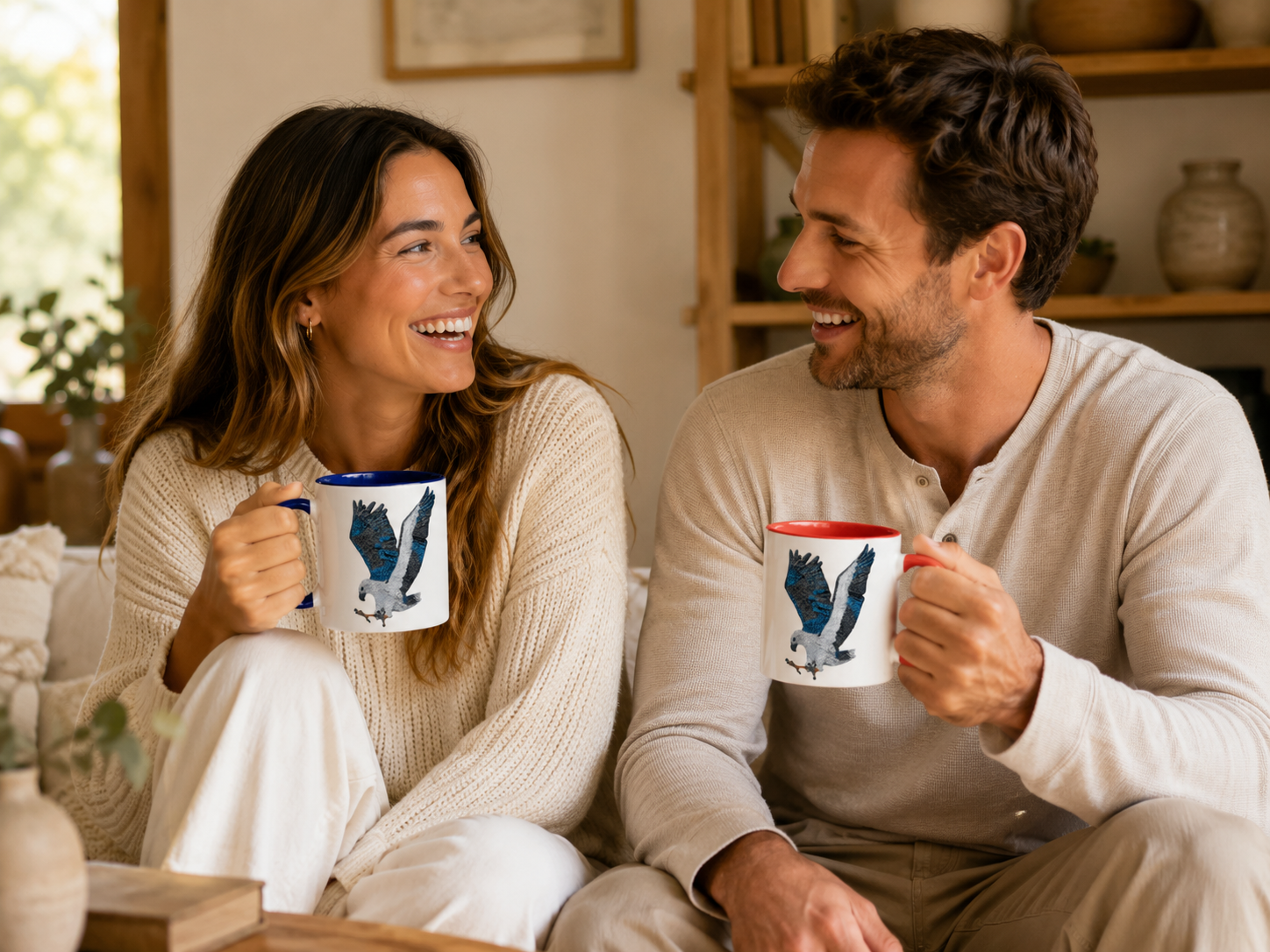 Two people laughing indoors while holding Willow White-bellied Sea Eagle mosaic mugs, showing the artwork clearly in a warm casual home setting with soft natural light.