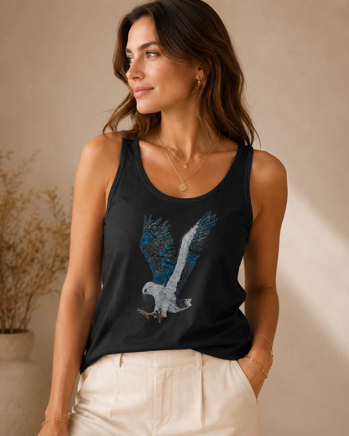 Fashion-style lifestyle image of a model wearing the Willow tank top with relaxed trousers, layered jewellery, and warm studio lighting, highlighting the sleeveless white garment, artist-designed Willow artwork, and elegant everyday styling for Australian wearable art clothing.
