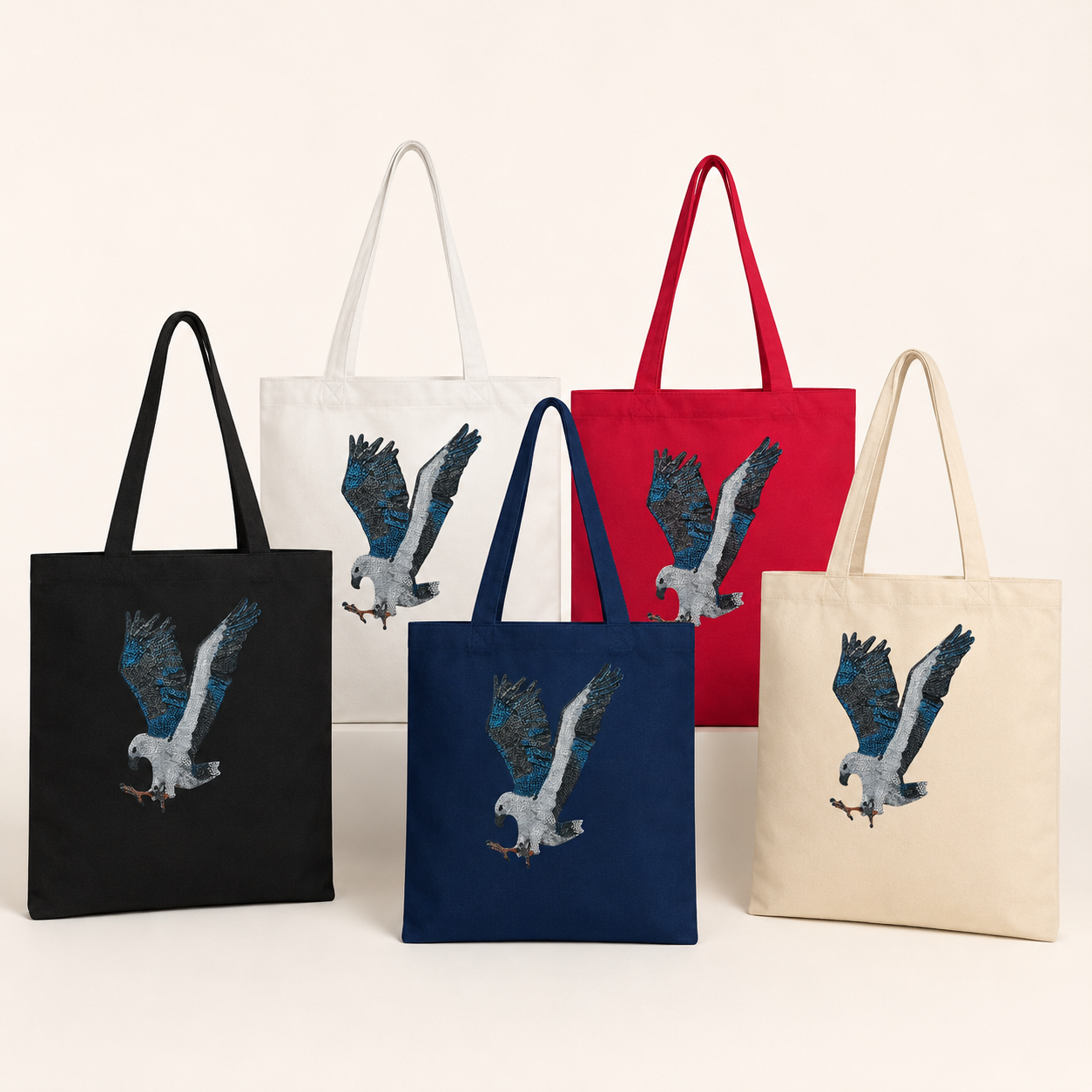 Collection of Willow White-bellied Sea Eagle mosaic tote bags displayed together in white, natural, black, navy blue, and red, arranged on a warm neutral studio background to show the full colour range of reusable cotton tote bags featuring Australian wildlife mosaic art.